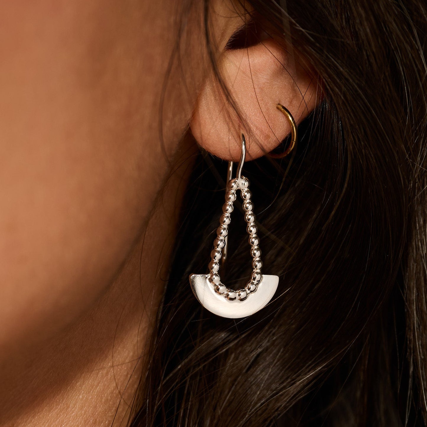 Close-up of a person wearing a silver earring with a half-circle design.