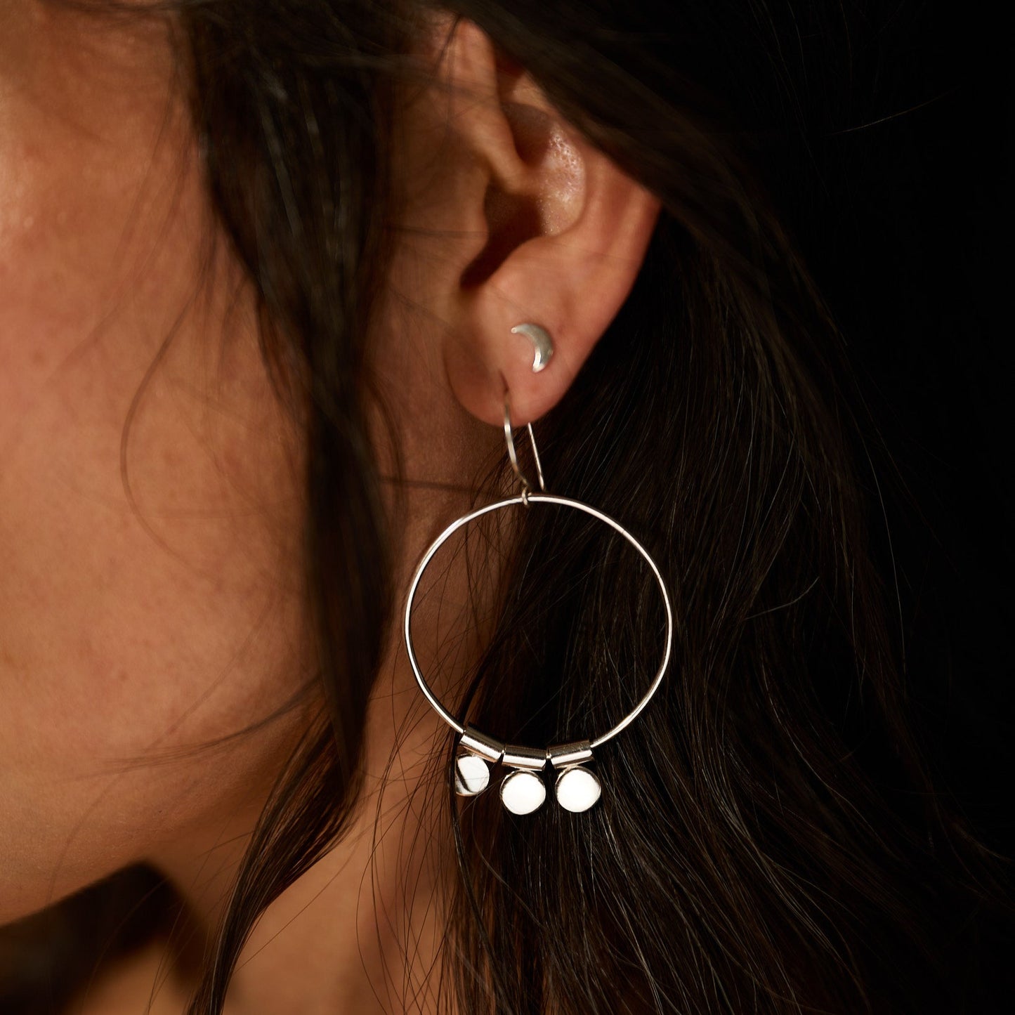Close-up of an ear wearing a silver hoop earring with small round charms.