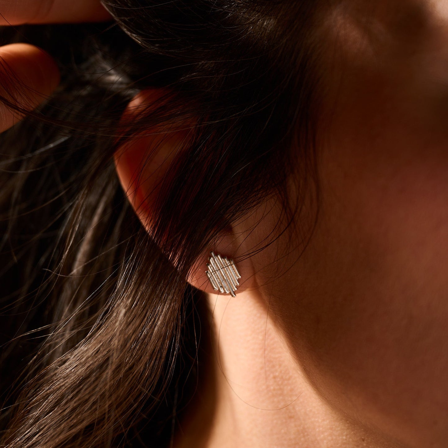 Close-up of an ear with a diamond earring, hair partially covering the face.