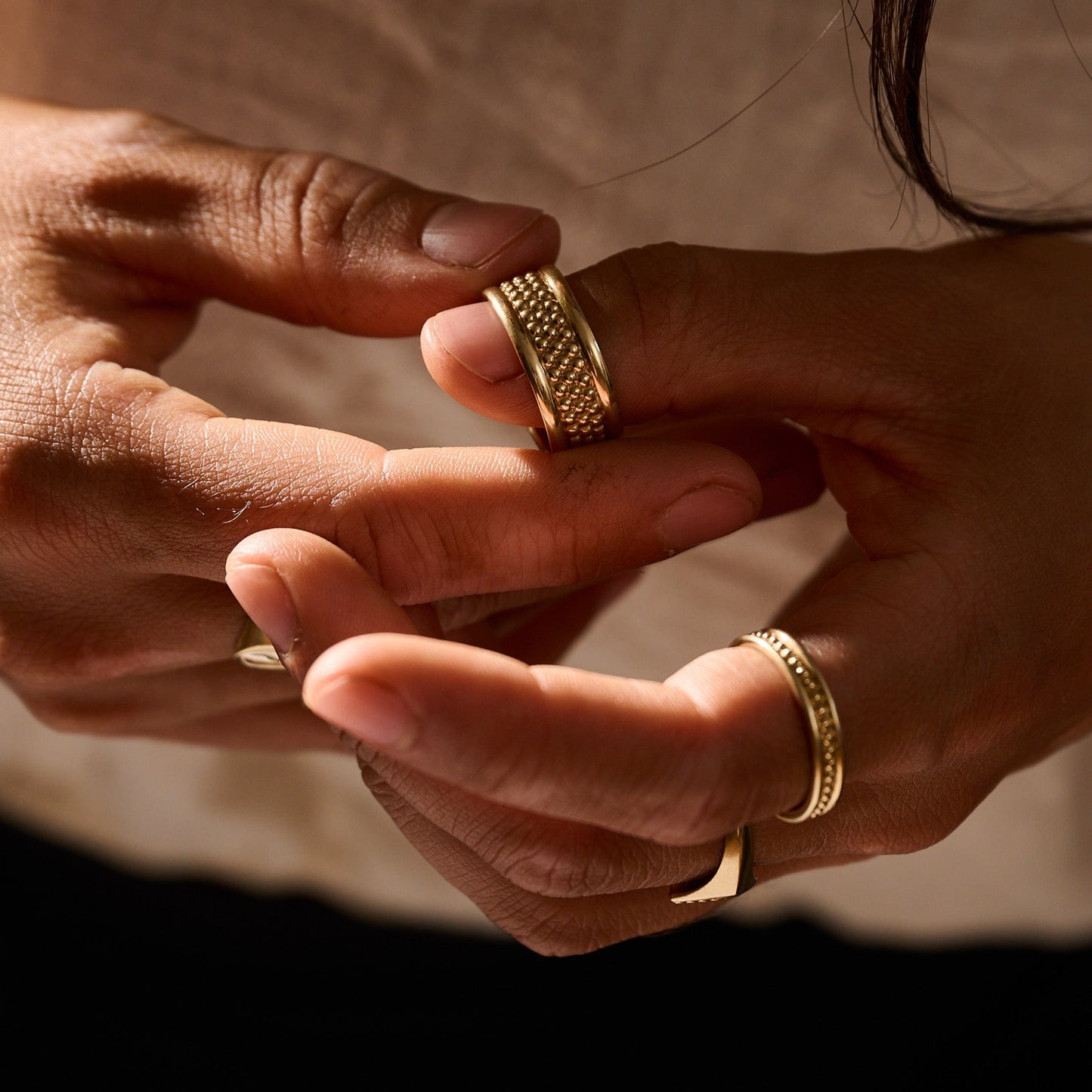 Close-up of two hands wearing gold rings against a neutral background