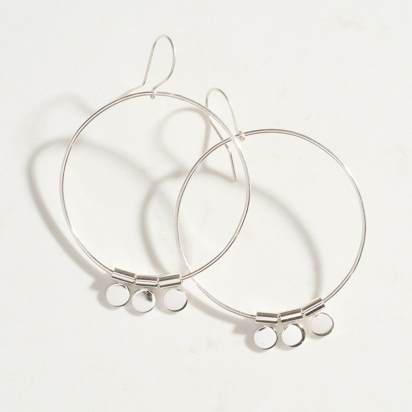 Silver hoop earrings with small round pendants on a white background
