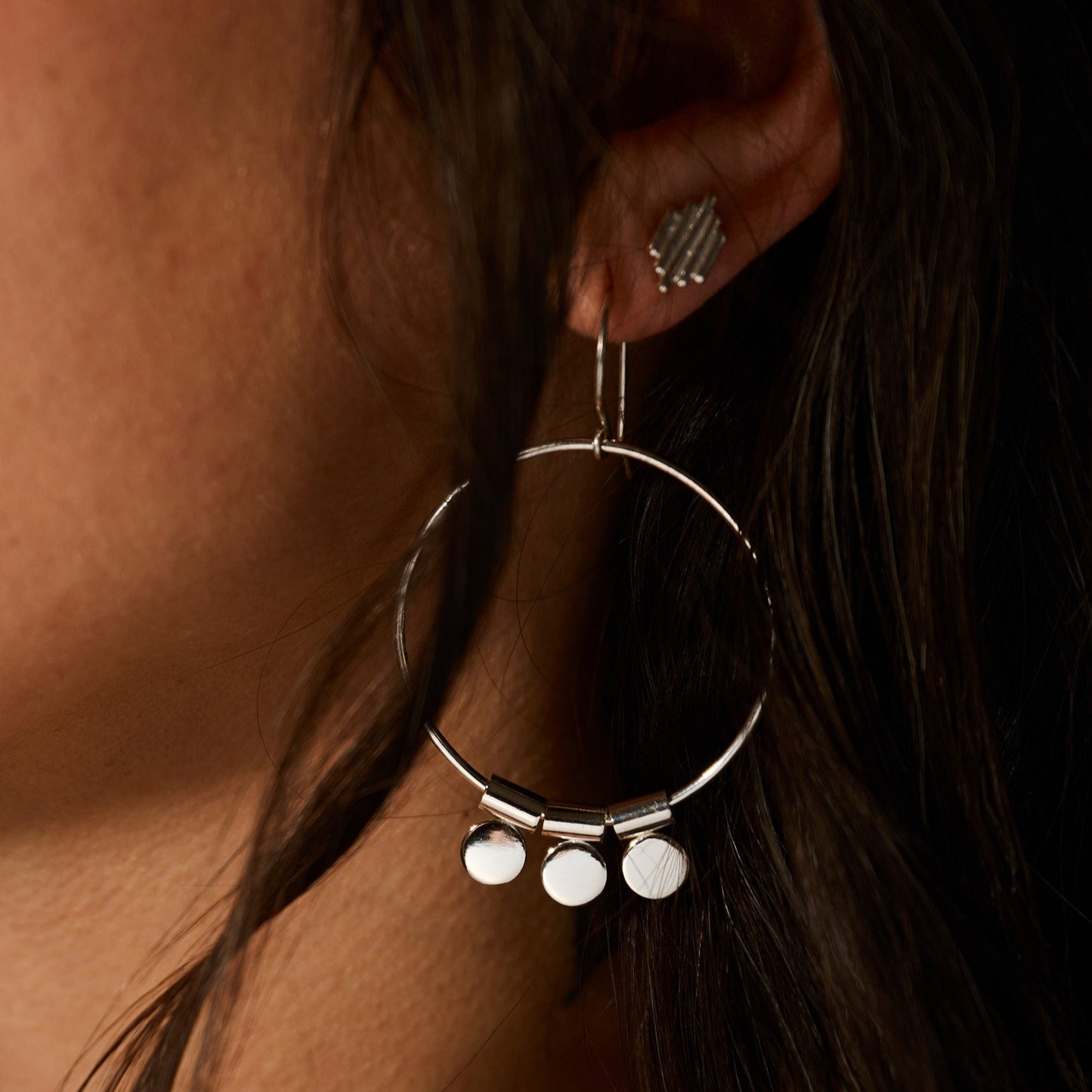 Close-up of a silver hoop earring with dangling charms worn by a person.