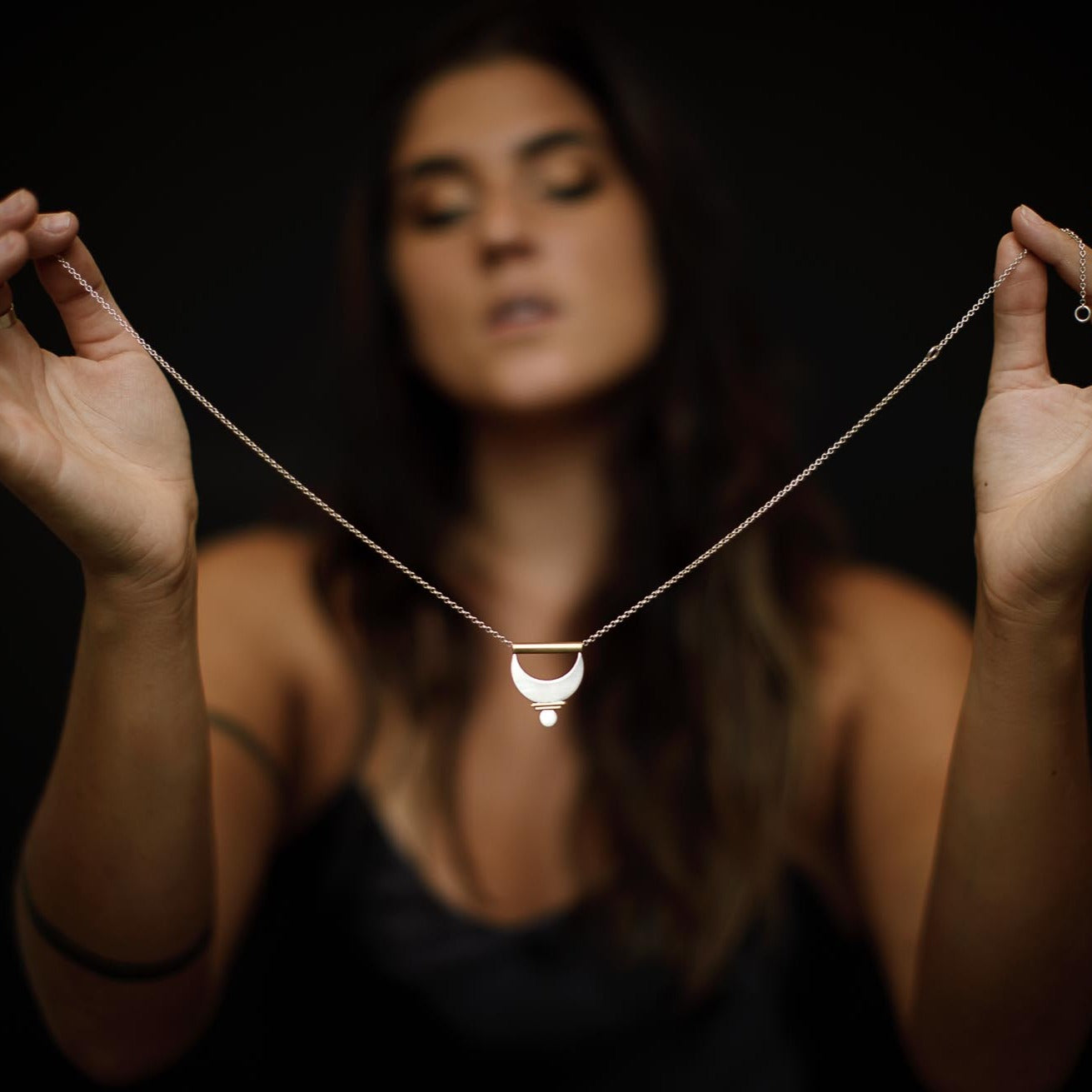 Holding up the Large Prana Pendant as if about to put it on.