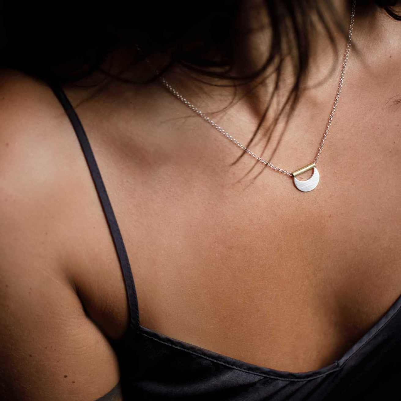 A silver crescent moon shaped necklace hangs from brass tubing that hangs from a silver chain.