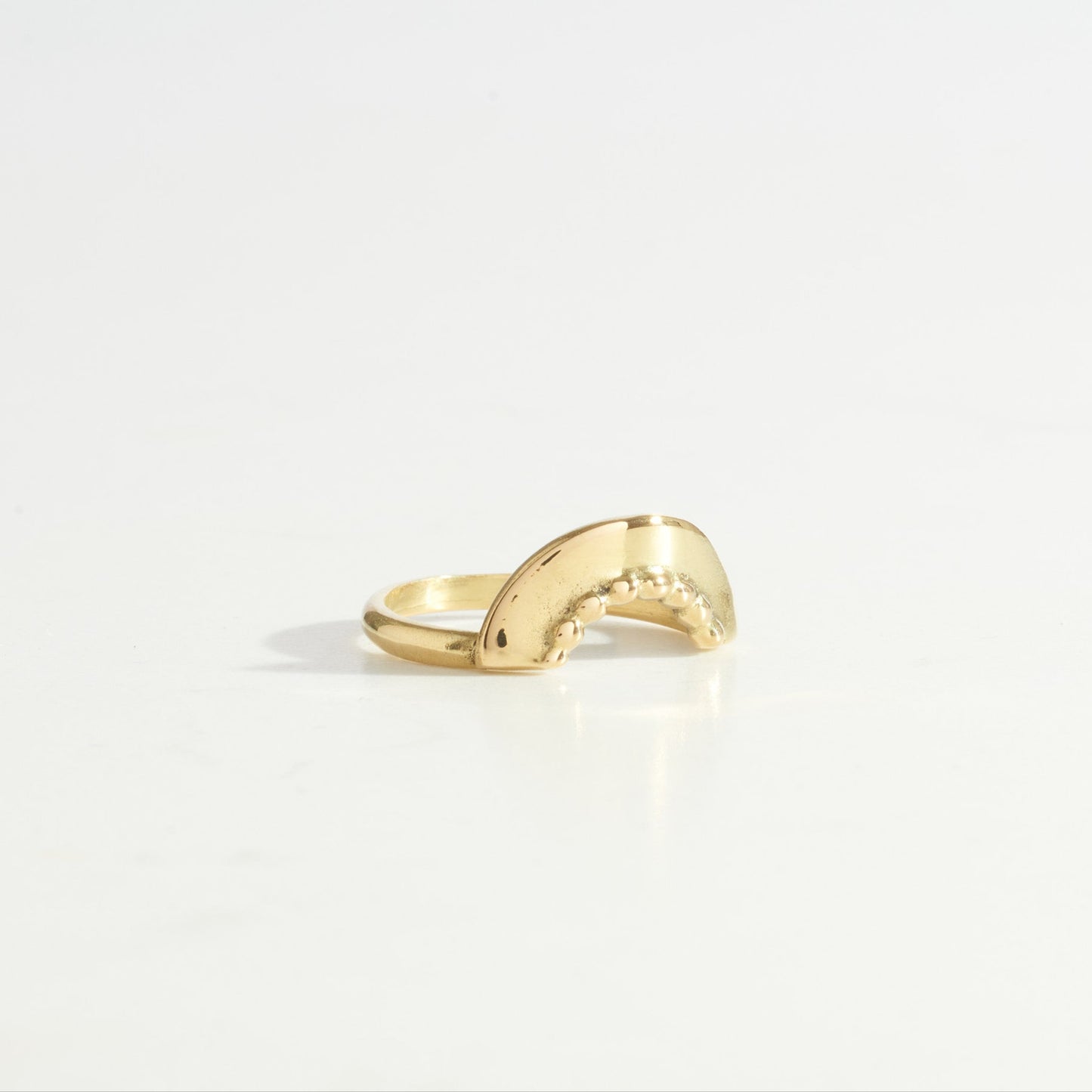 A gold ring with a curved design with a dotted texture to stack with stone ring on a white background. 