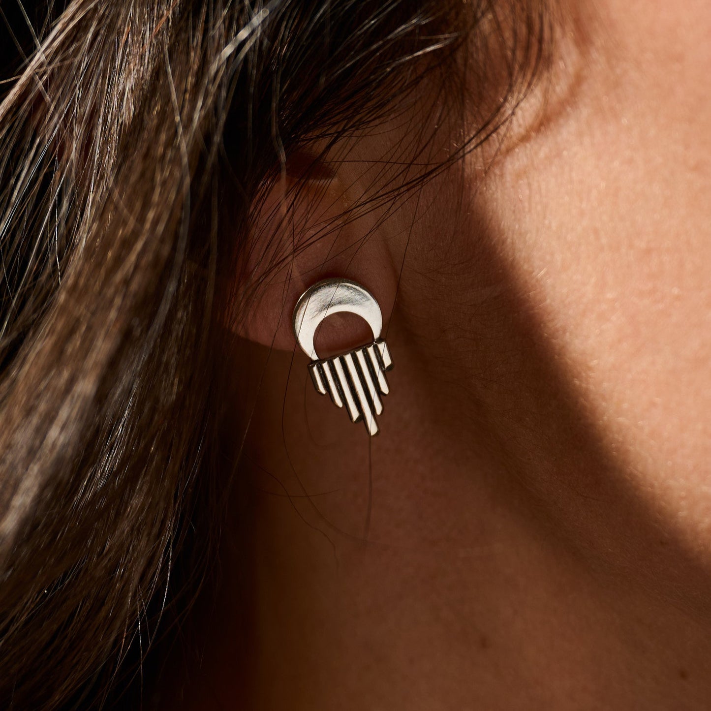 Silver earring worn on an ear with a blurred background
