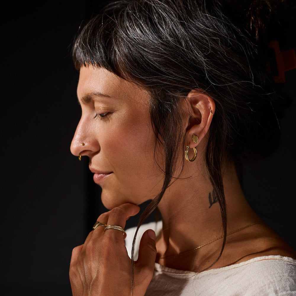 
                      
                        Woman with tied back dark hair wearing gold hoop earrings against a black background
                      
                    