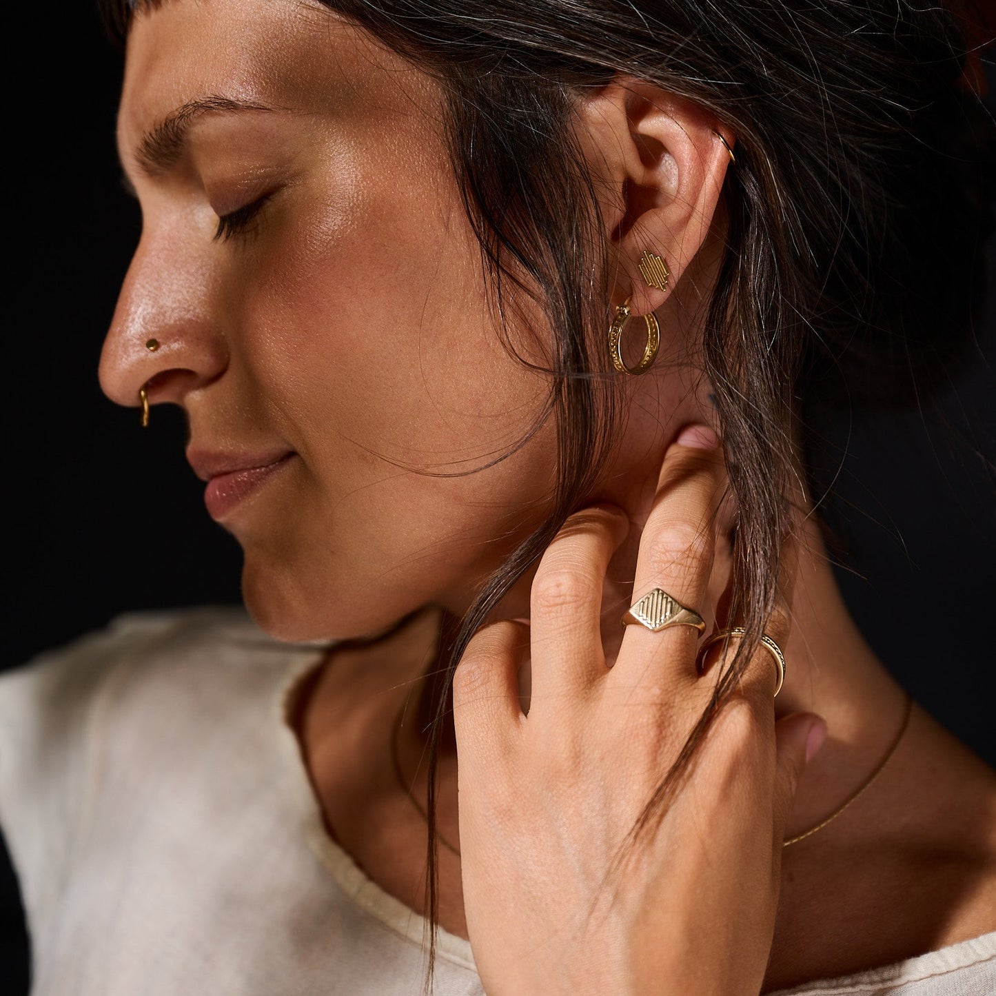 Close-up of a woman wearing gold earrings and rings against a dark background