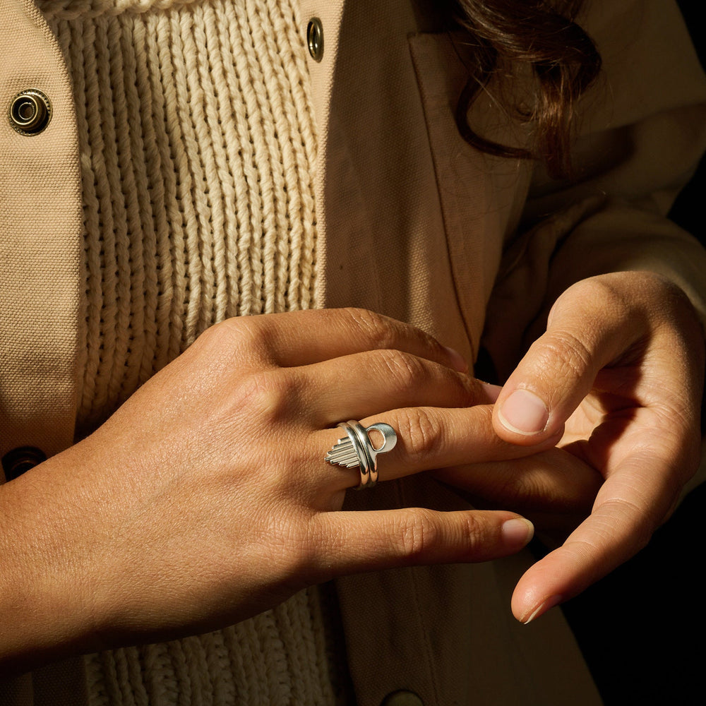 
                      
                        Close-up of a person wearing a ring with a beige coat and textured fabric background
                      
                    