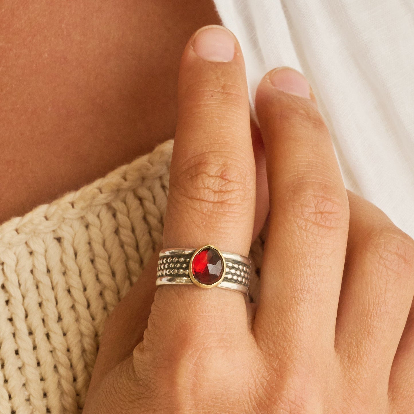 Hand wearing a ring with a red gemstone on a textured surface