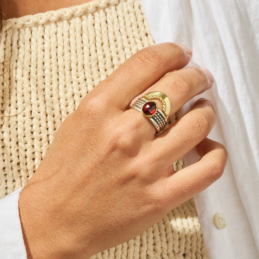 
                      
                        Hand wearing a gold ring with a red gemstone, holding a woven beige bag.
                      
                    