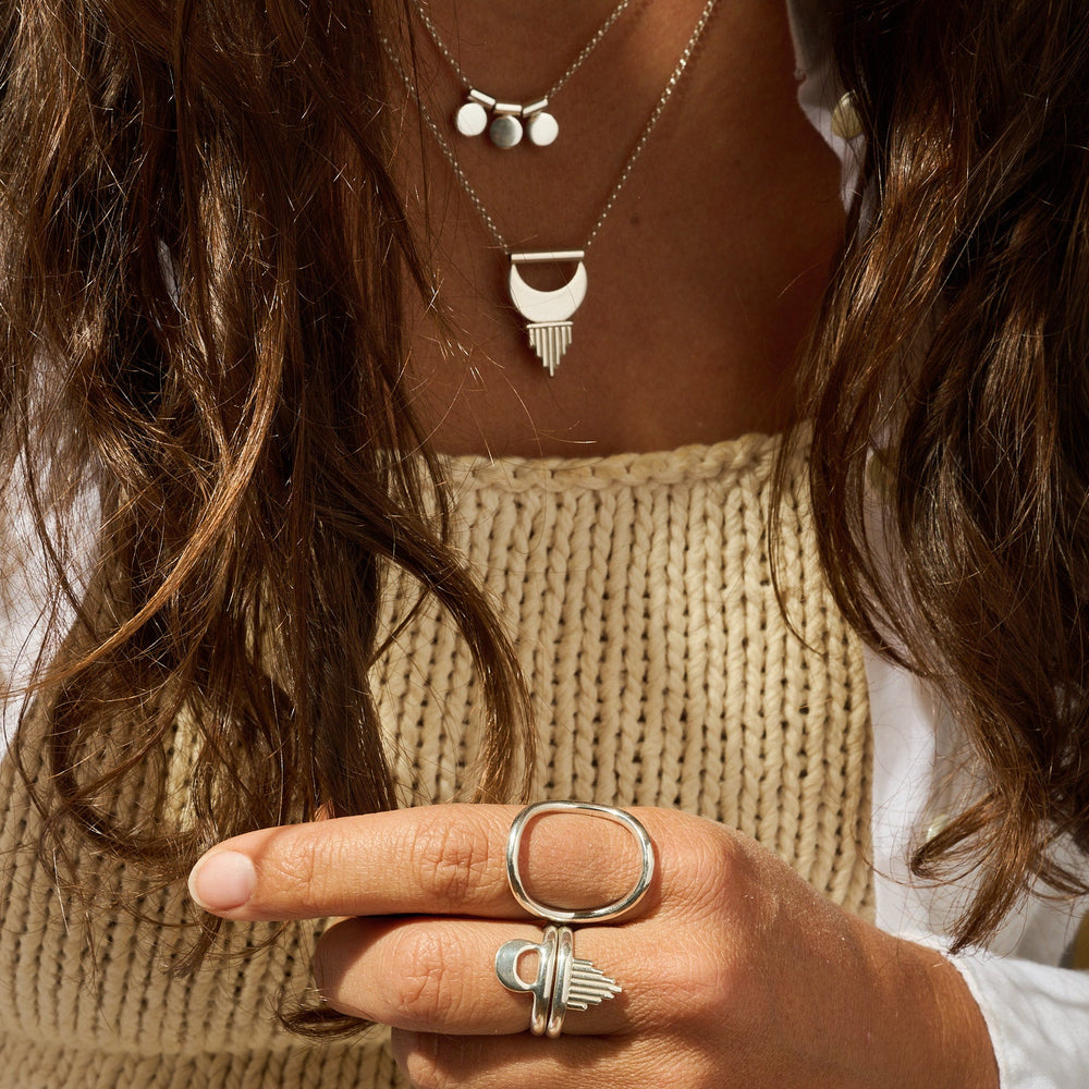 
                      
                        Close-up of a person wearing layered necklaces and rings with a neutral background
                      
                    