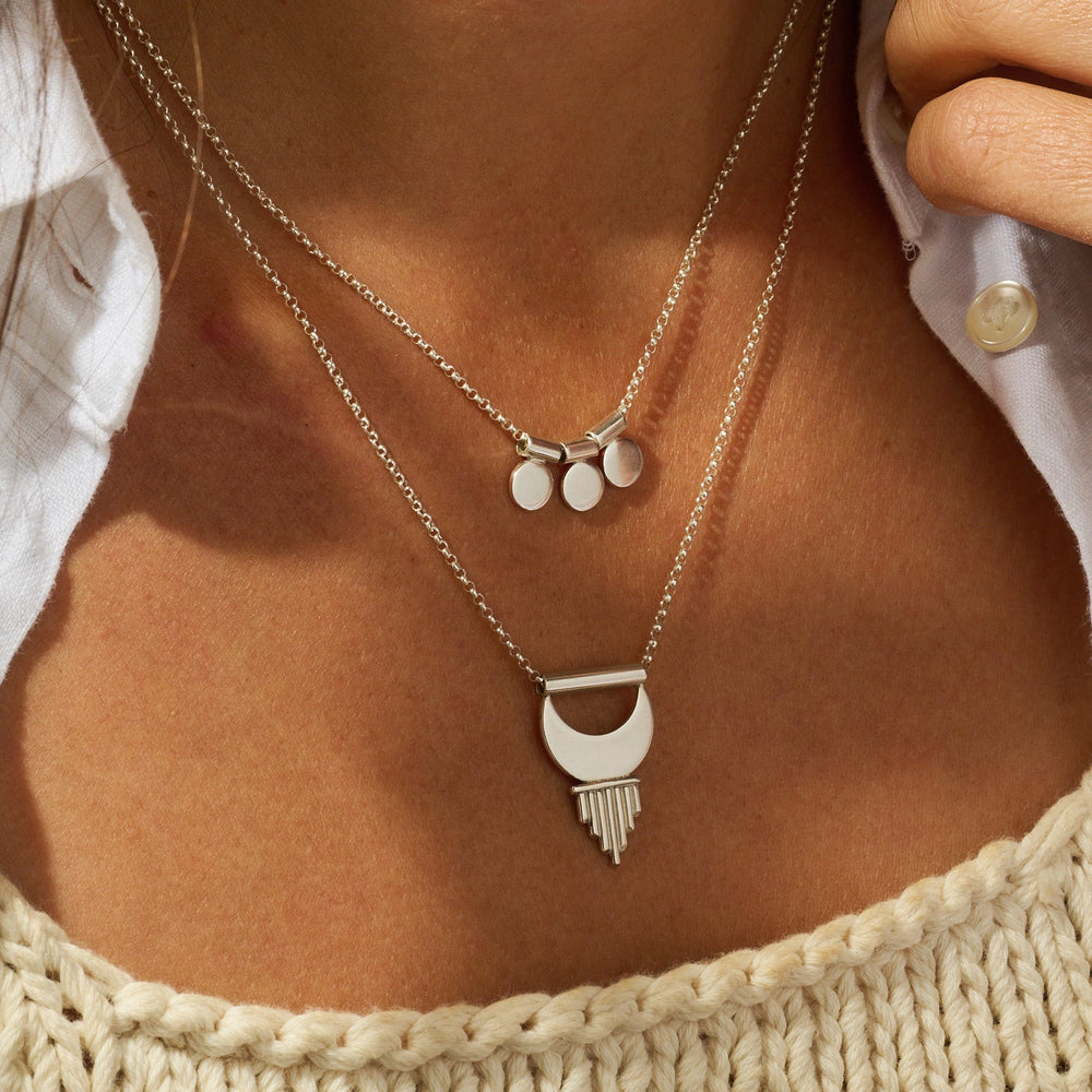 
                      
                        Close-up of a person wearing layered silver necklaces with a textured top.
                      
                    