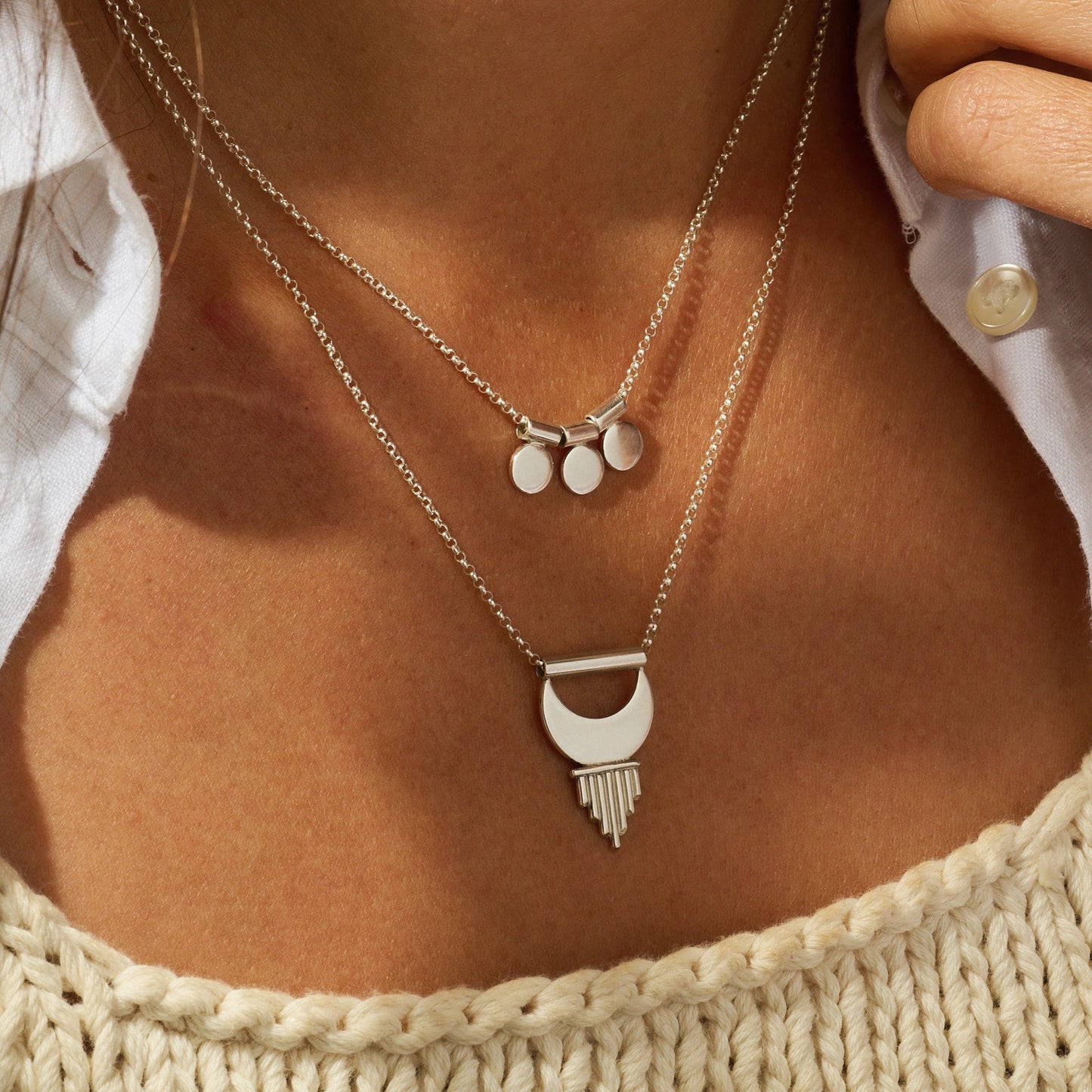Close-up of a person wearing layered silver necklaces with a textured top.