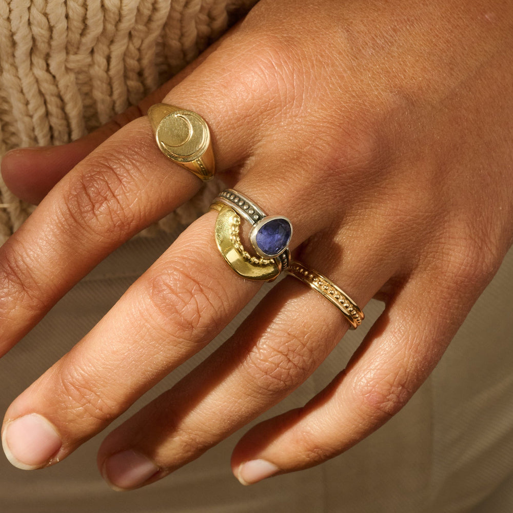 Hand wearing two gold rings with a blue stone on a neutral background