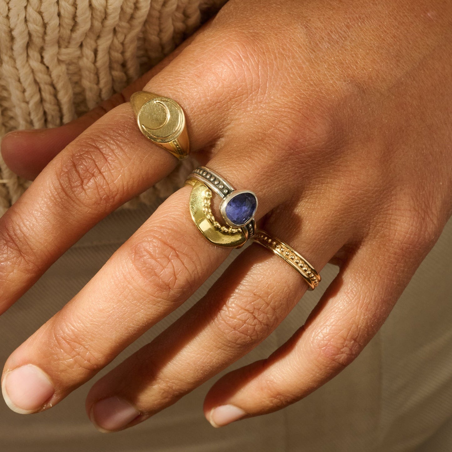 Hand wearing two gold rings with a blue stone on a neutral background