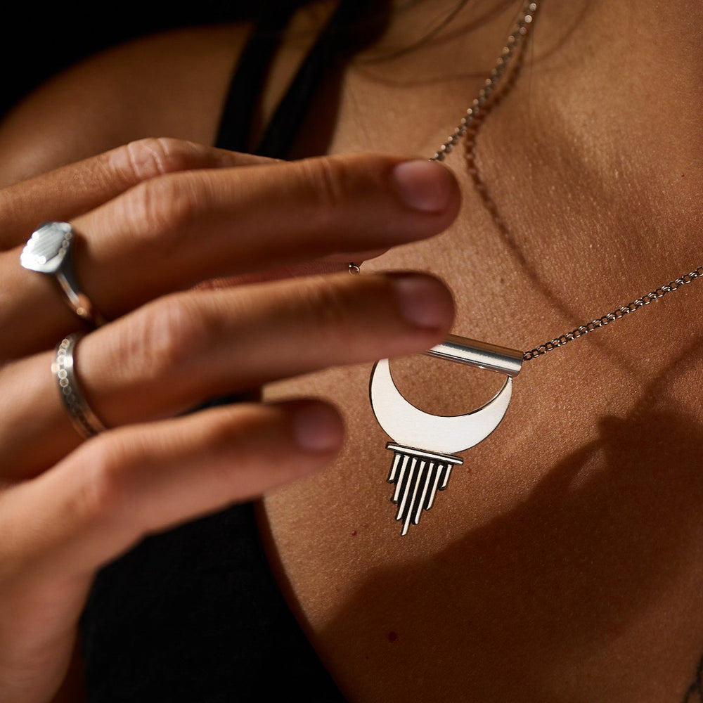 Person wearing a silver necklace with a crescent moon pendant, holding a silver ring.