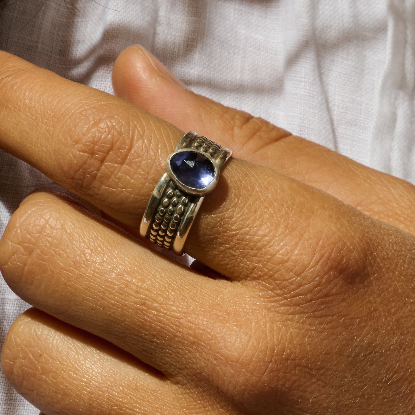Silver ring with a blue gemstone on a person's finger against a white background