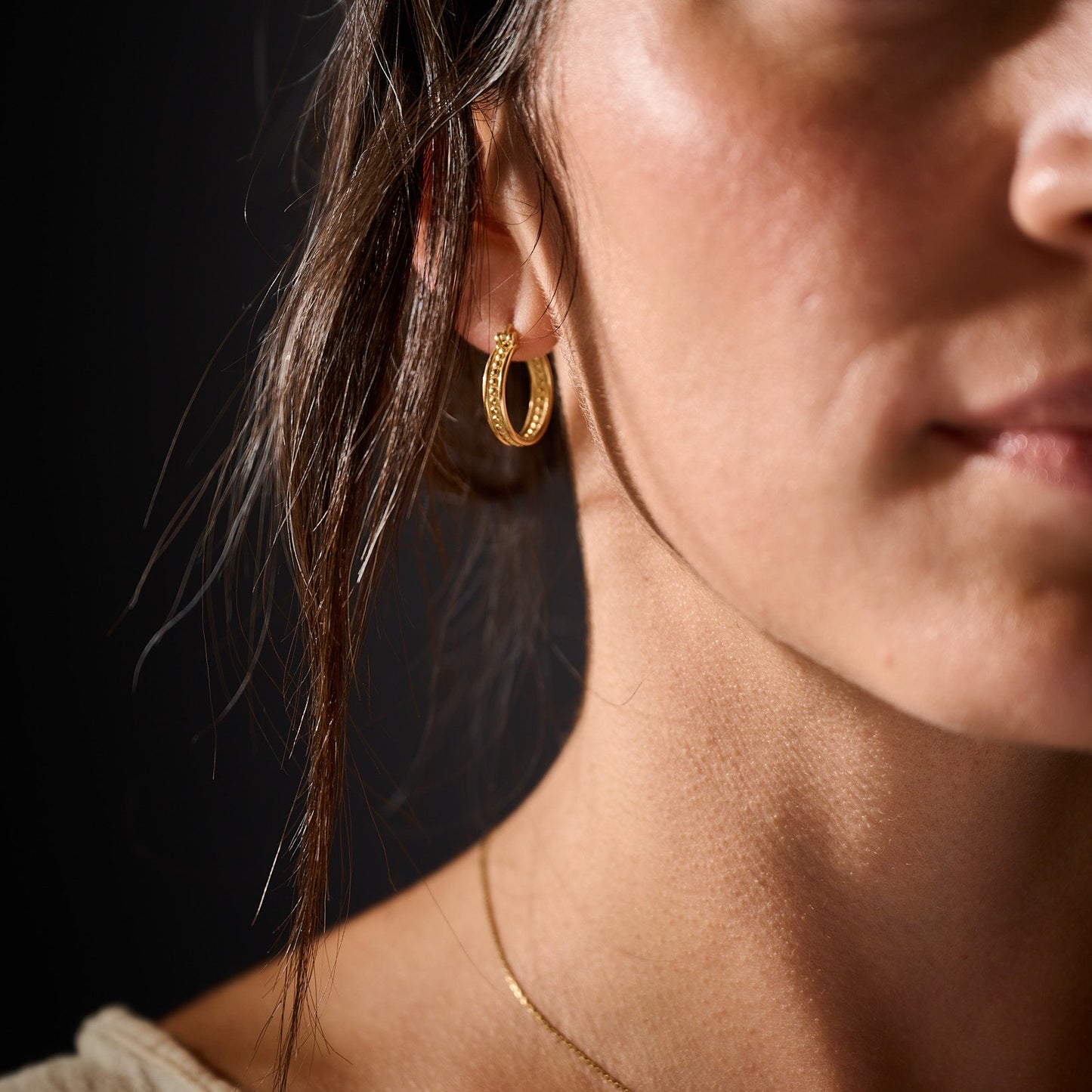 Close-up of a person wearing gold hoop earrings with a dark background
