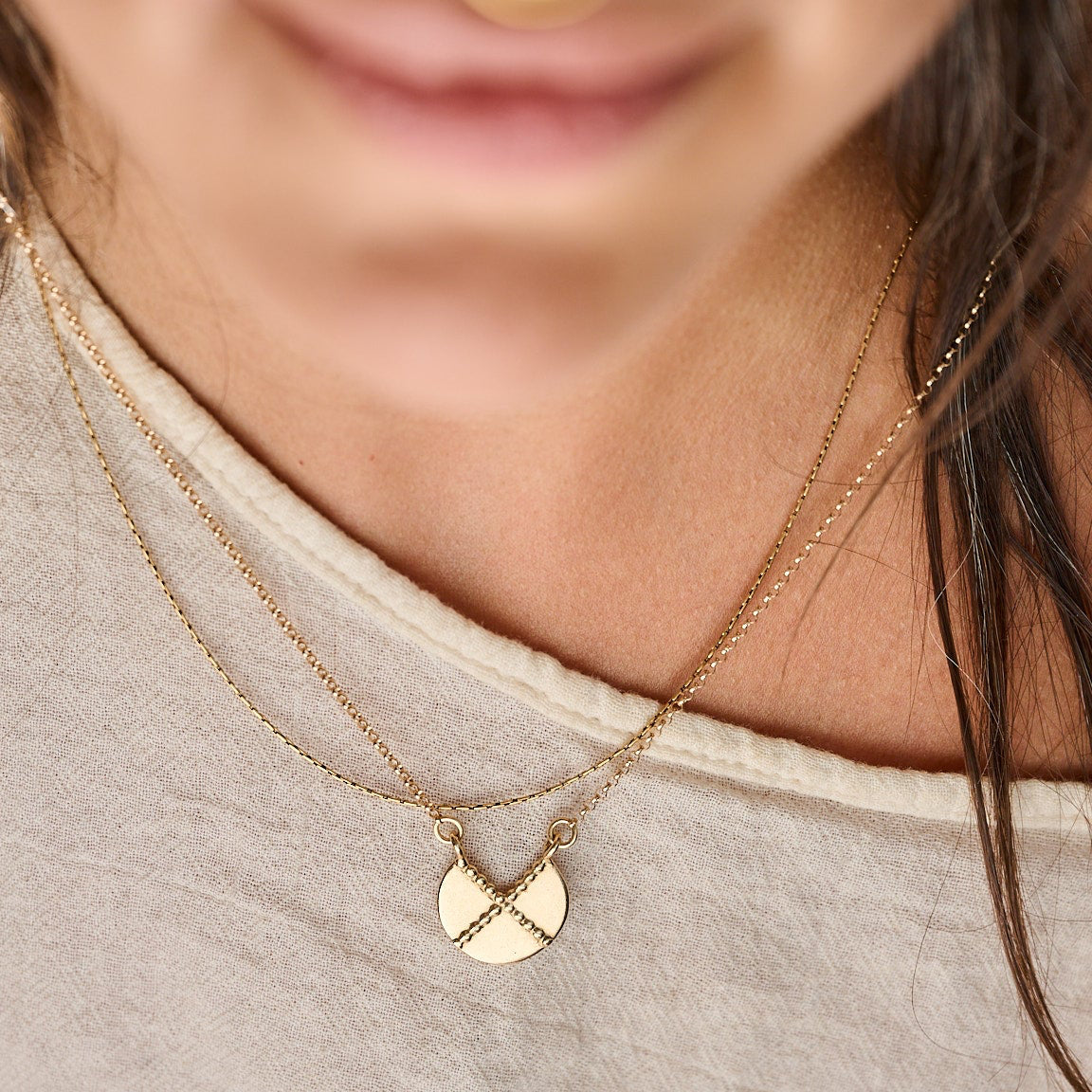 Close-up of a person wearing a gold shield necklace with a dotted motif that cross like an x. 