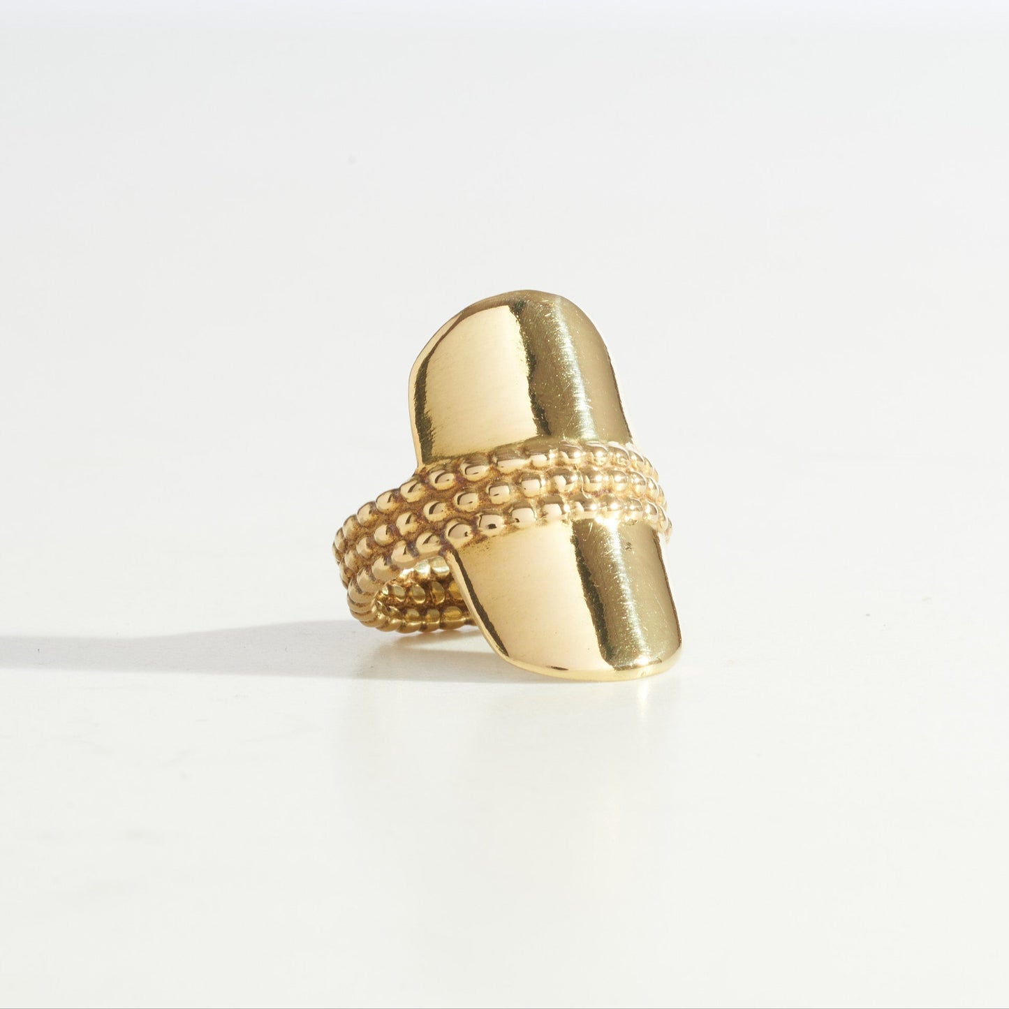 A gold ring with a bold, shield-like design, featuring a textured band and a smooth, curved central piece.