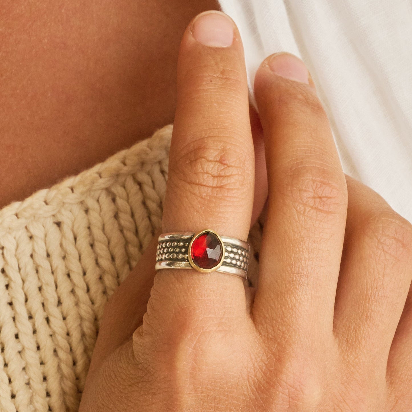 Hand wearing a ring with a red gemstone on a textured surface