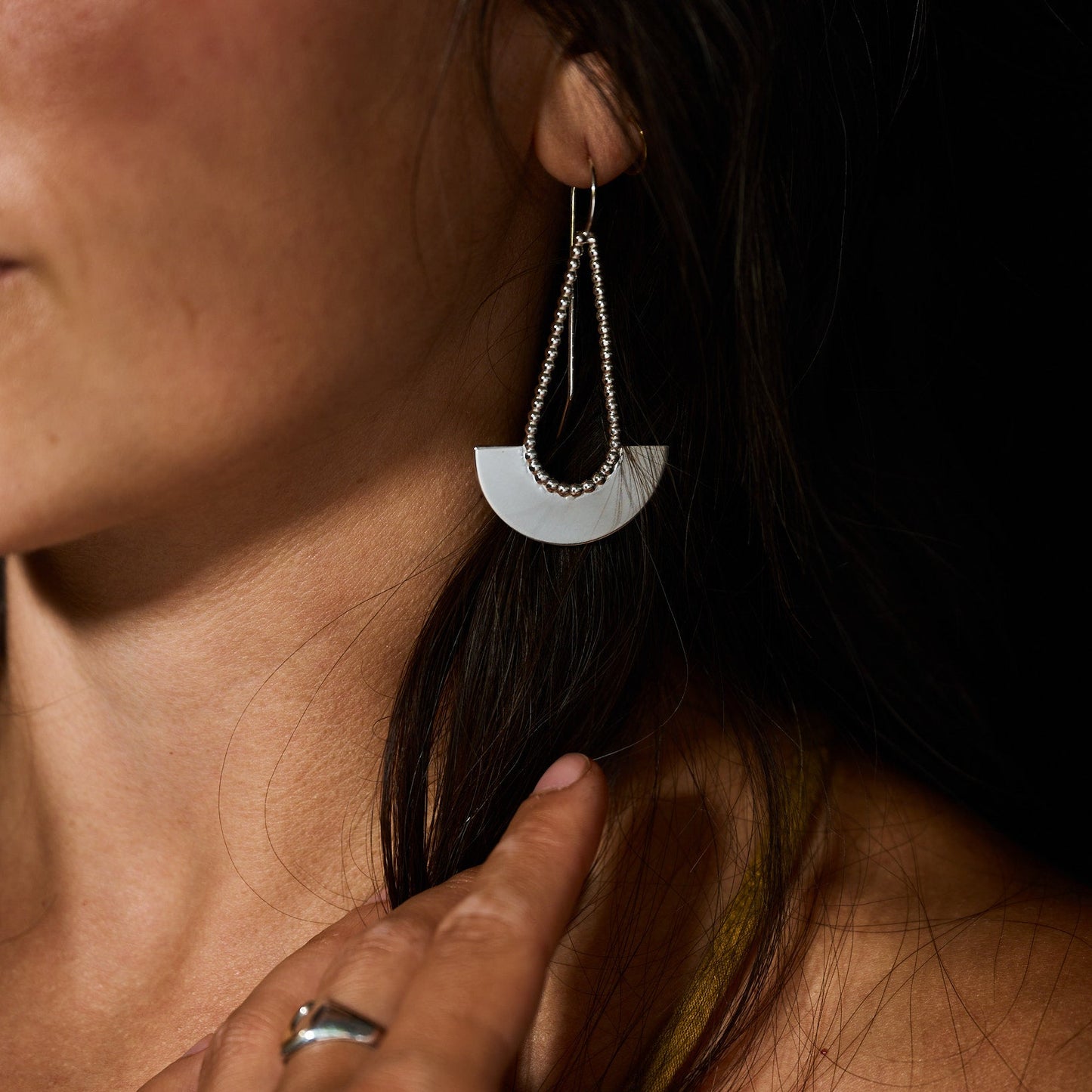 Close-up of a person wearing a modern, silver earring with a dark background