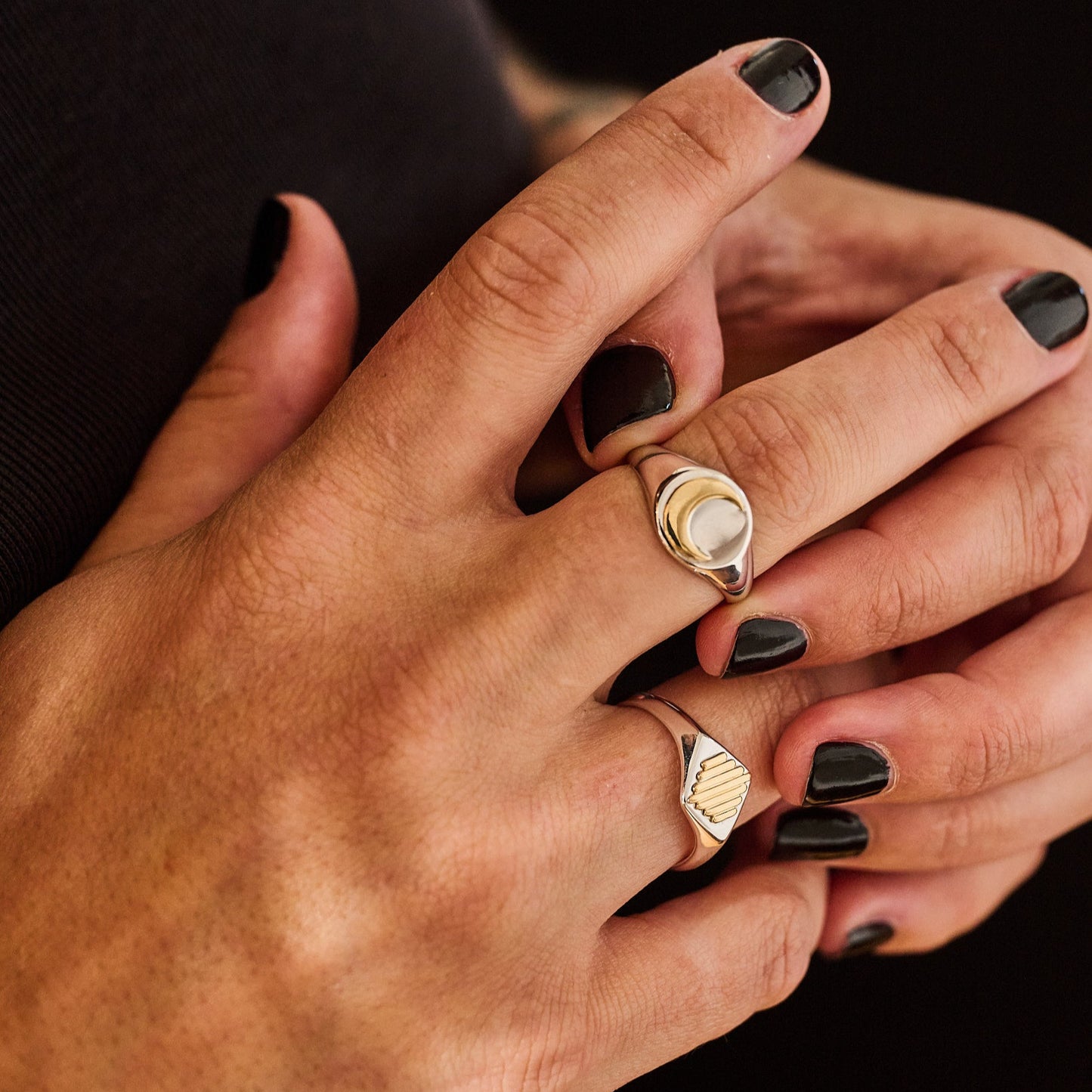 Close-up of a hand wearing silver signet rings with gold sun ray and moon symbols