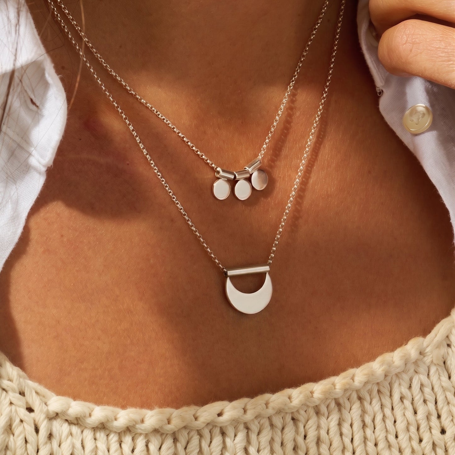 Close-up of a person wearing two silver necklaces with circular pendants.
