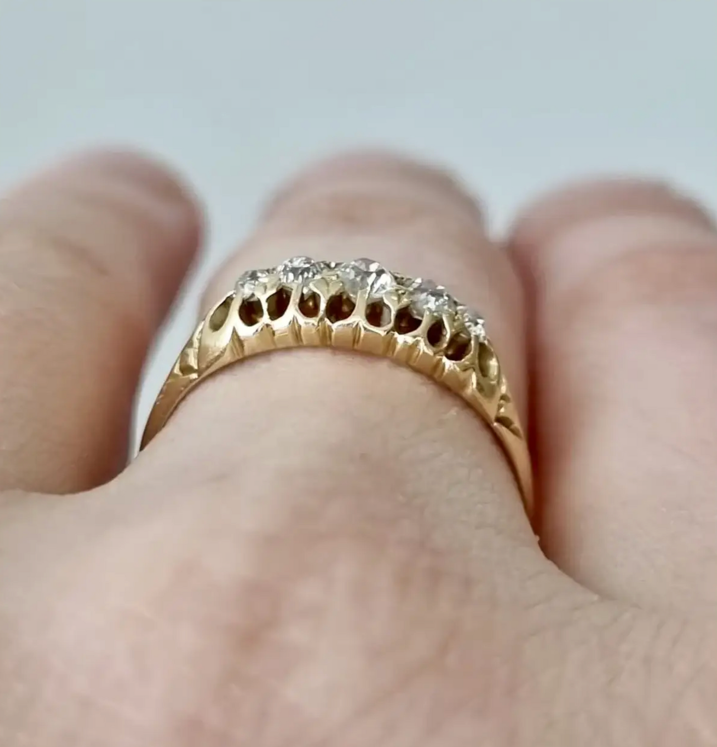 Gold ring with diamonds on a finger against a neutral background