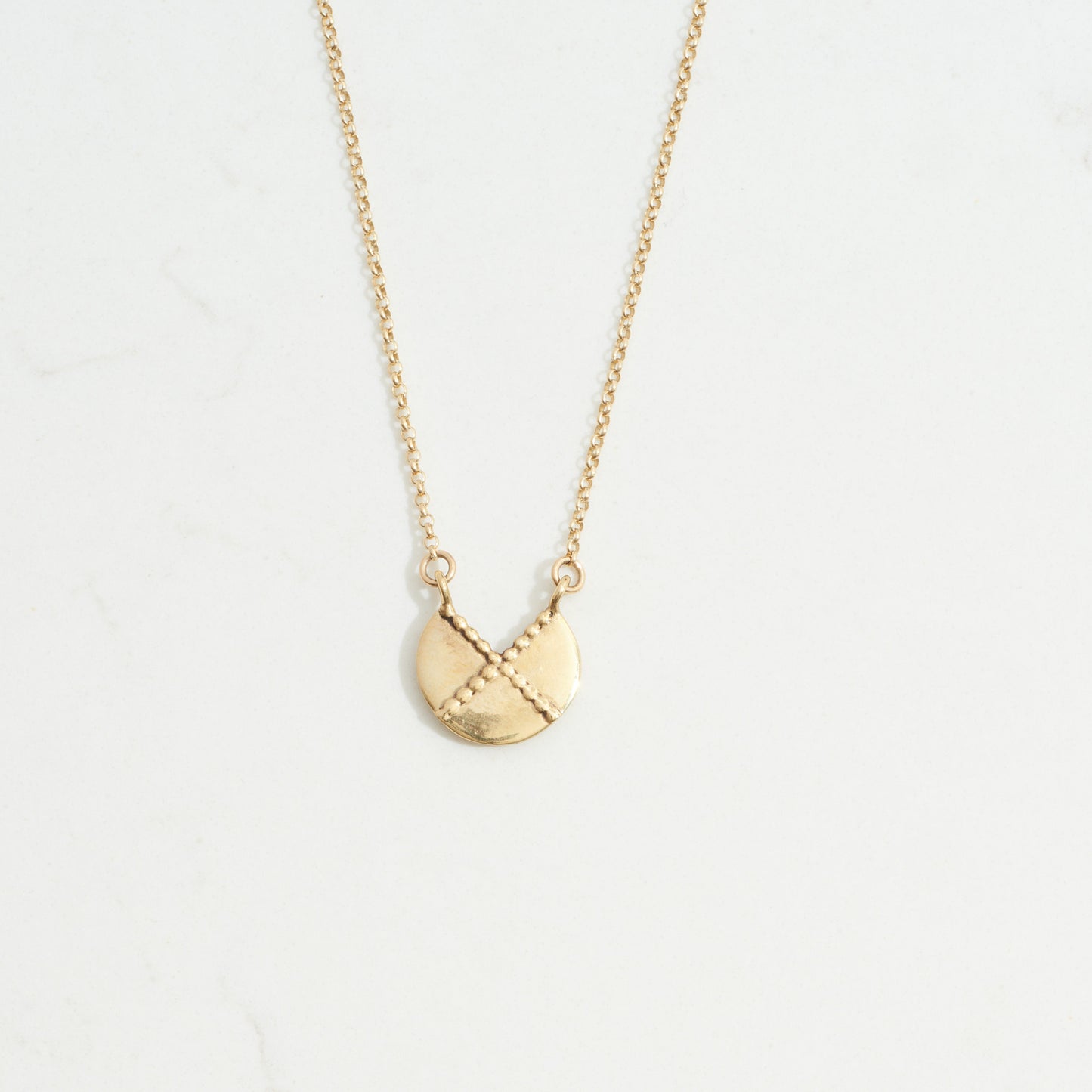 Gold circular pendant with intersecting dotted lines crossing in the shape of an "x" suspended from a thing gold chain