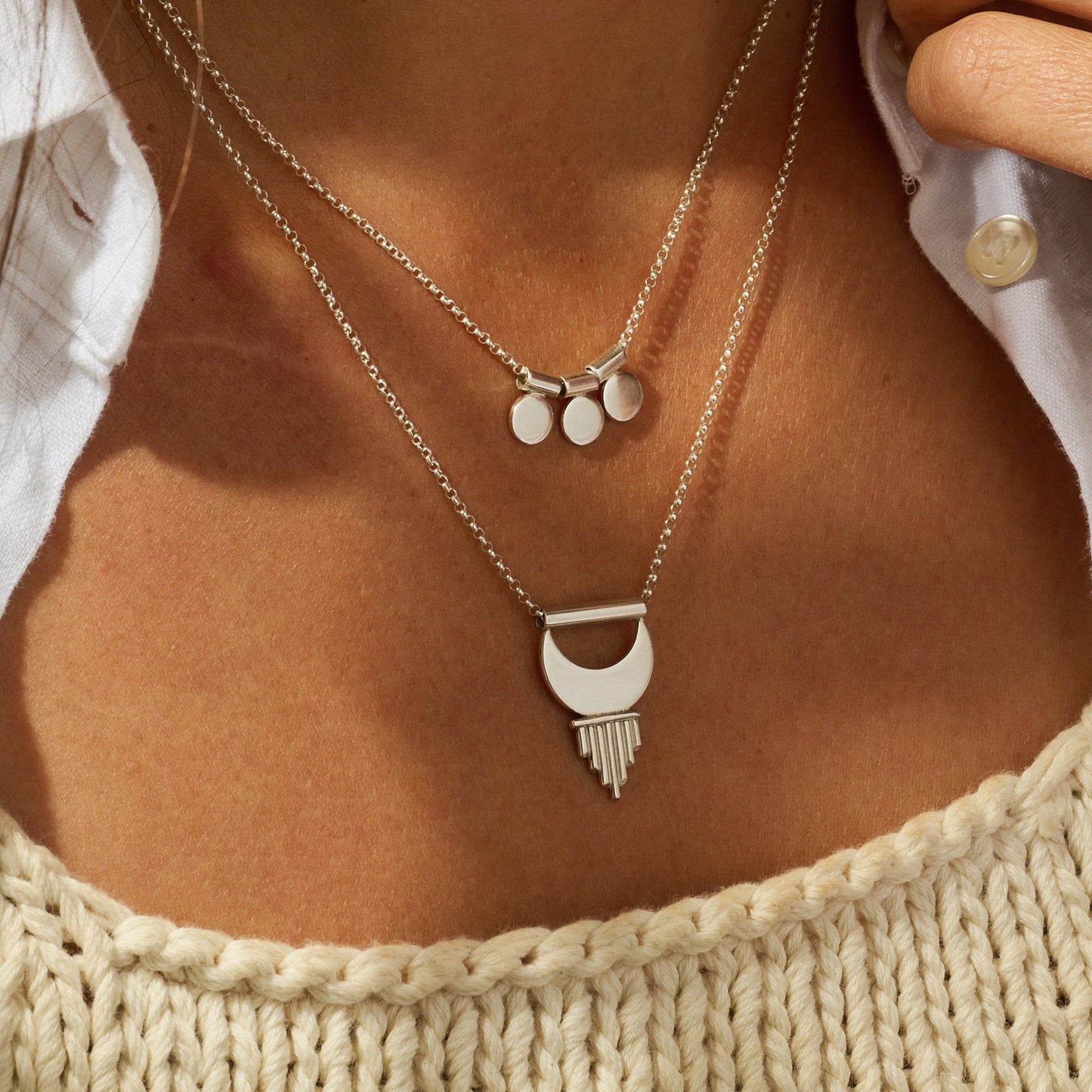 Close-up of a person wearing layered silver necklaces with a textured top.