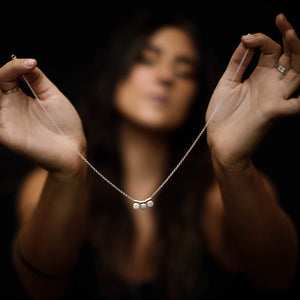 
                  
                    Holding a dainty, feminine necklace with three silver circle charms that dangle from yellow brass tubing hung on a silver chain.  
                  
                