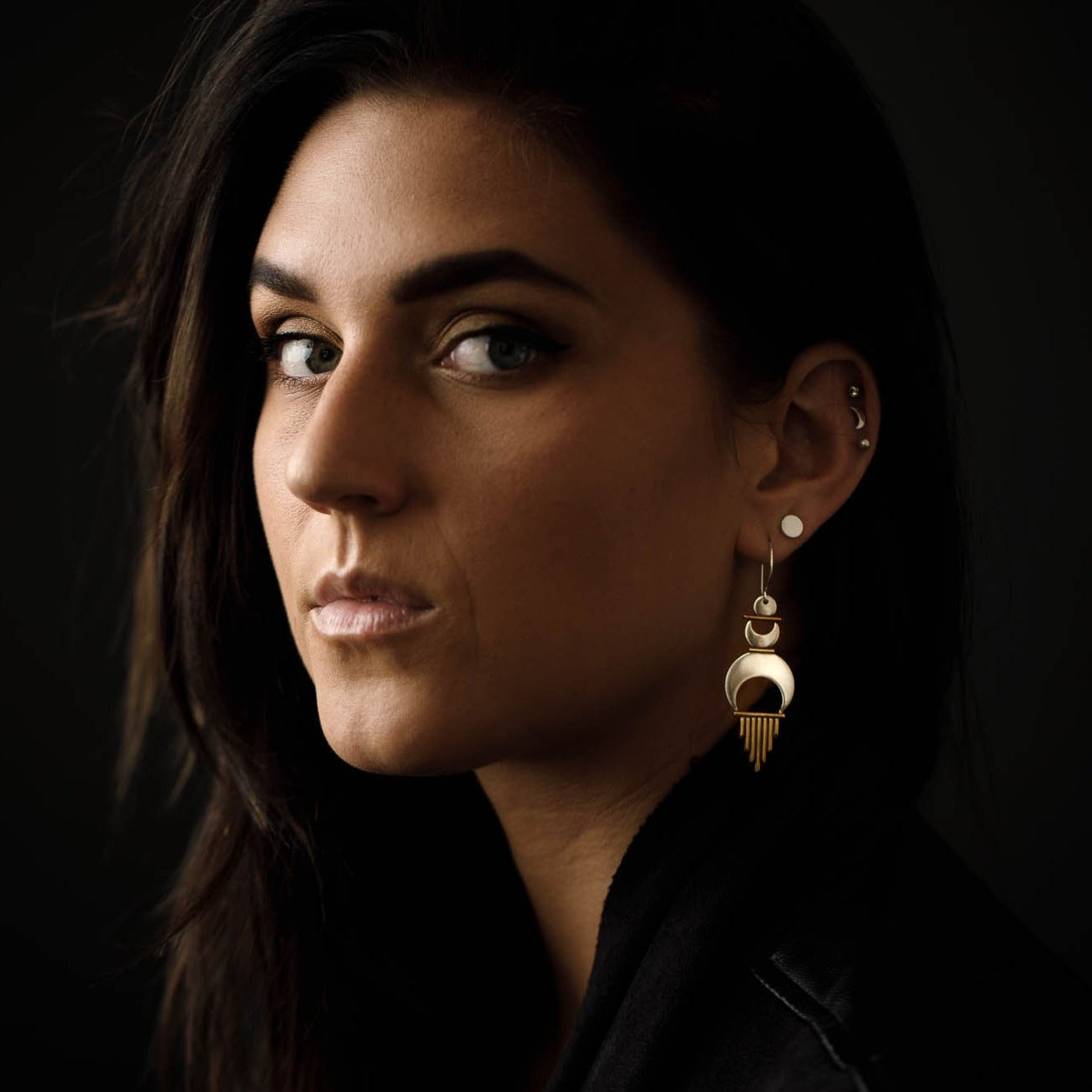 Beautiful girl with dark features turns to look at us while wearing the Alchemy Earrings. 
