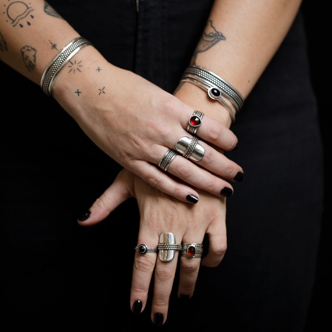 Two hands crossed wearing and assortment of silver textured rings and bracelets